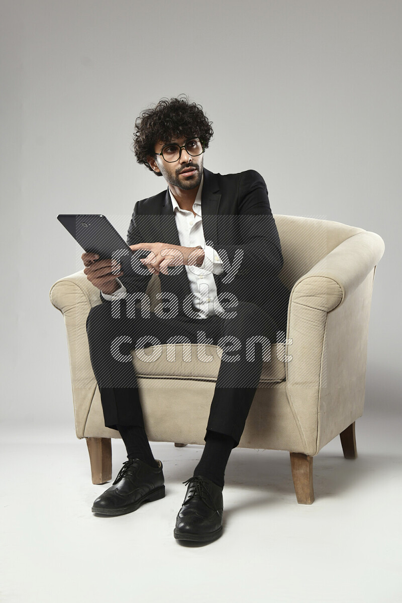 A man wearing formal sitting on a chair browsing on a tablet on white background