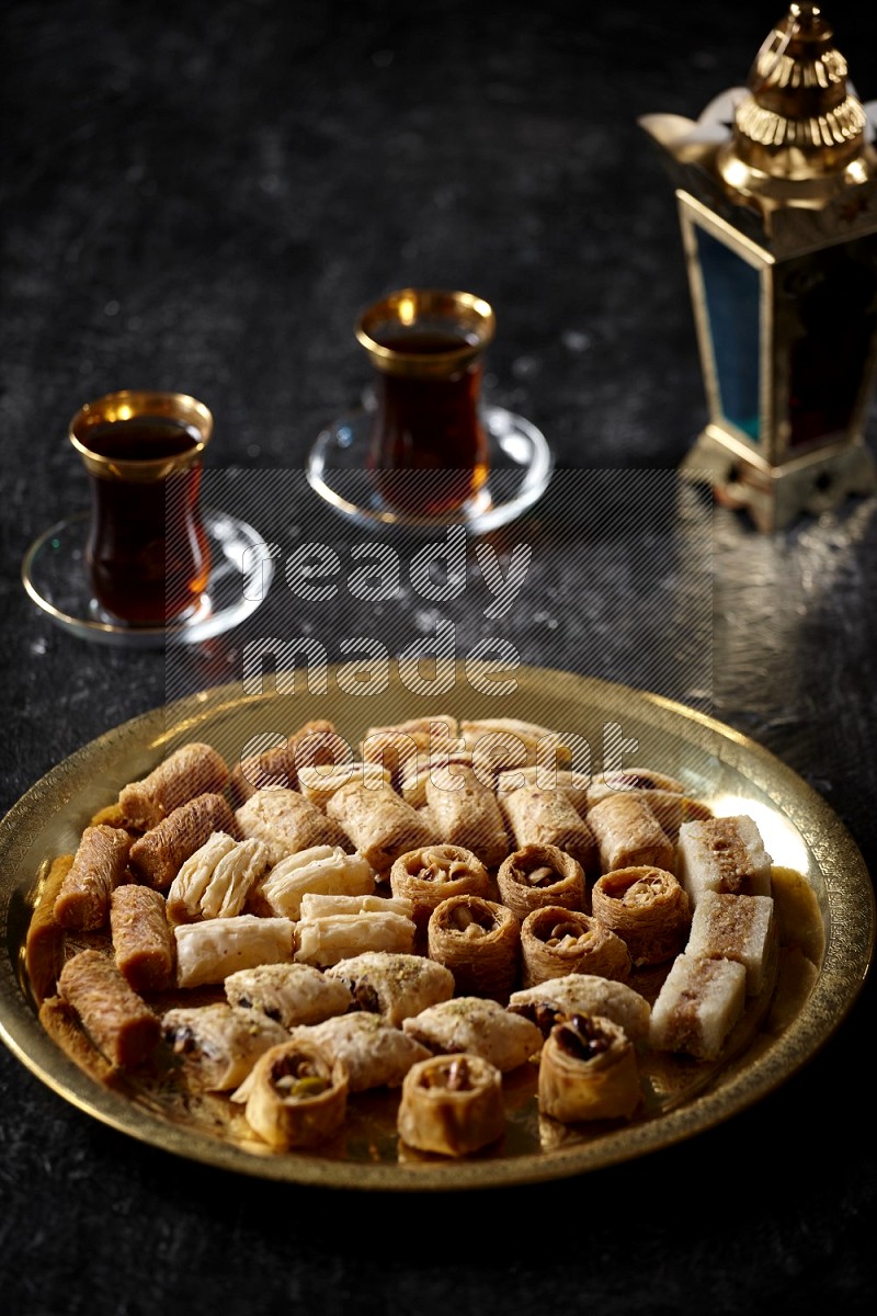 حلويات شرقية مع الشاي وفانوس معدني علي خلفية سوداء خشبية