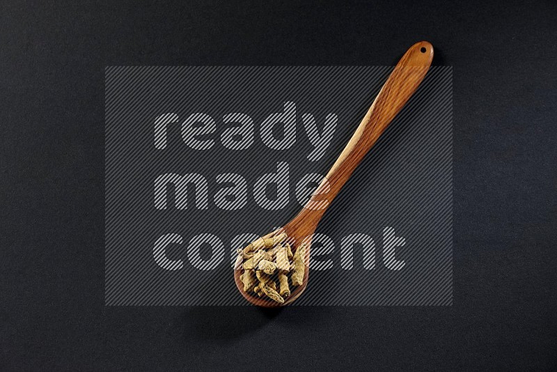 A wooden ladle full of dried turmeric fingers on black flooring
