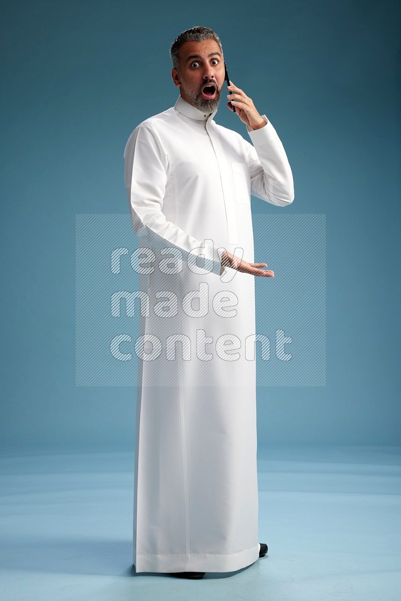 Saudi man wearing thob talking on the phone on blue background