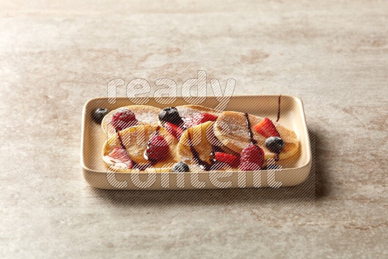 Five stacked mixed berries mini pancakes in a rectangular plate on beige background