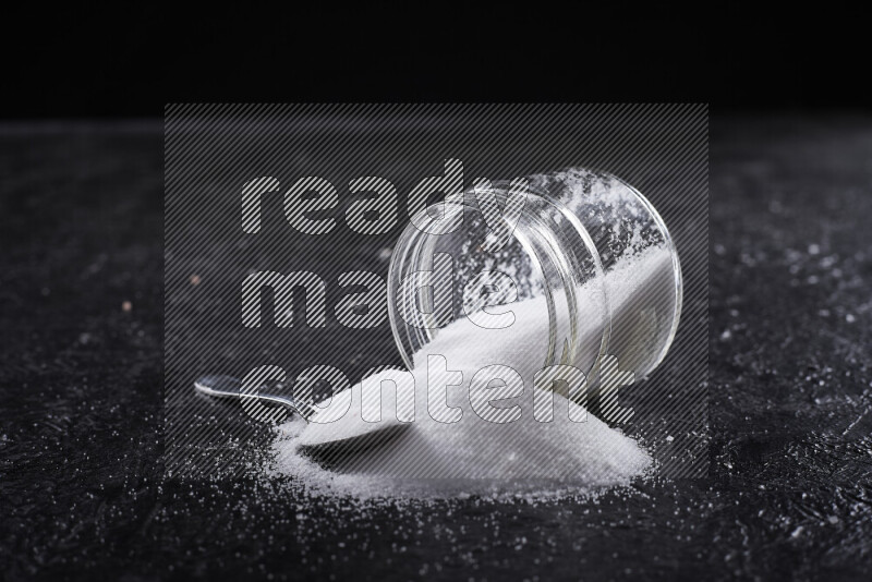 A glass jar full of fine table salt on black background