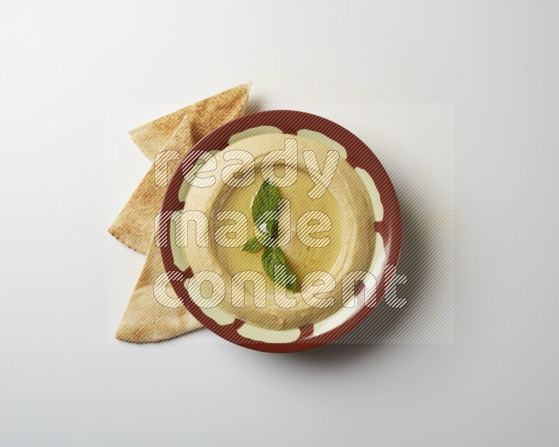 Hummus in a traditional plate garnished with mint on a white background