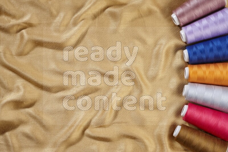 بكرات خيوط الخياطة متعددة الألوان على خلفية من القماش الأصفر