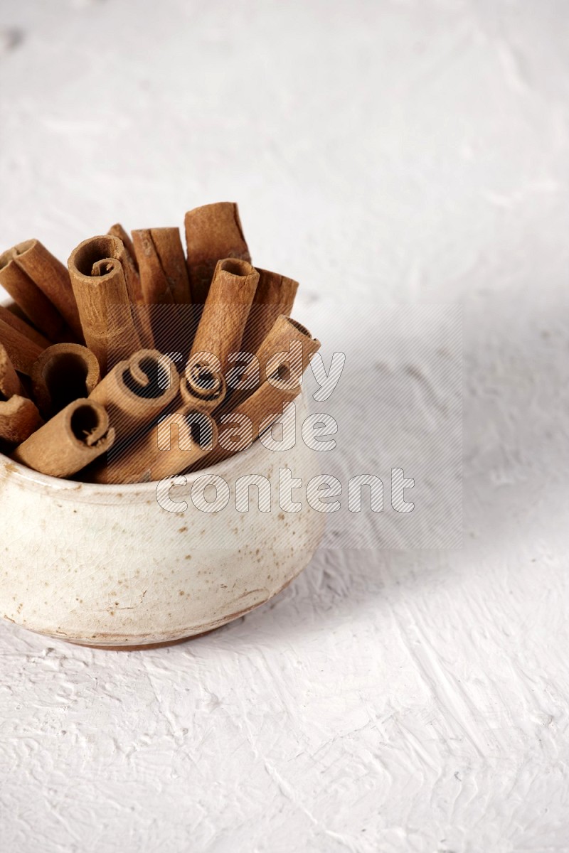 Cinnamon sticks in a beige bowl on a white background