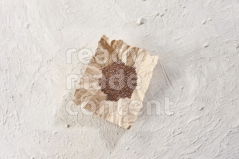 A crumpled piece of paper full of flax seeds on a textured white flooring