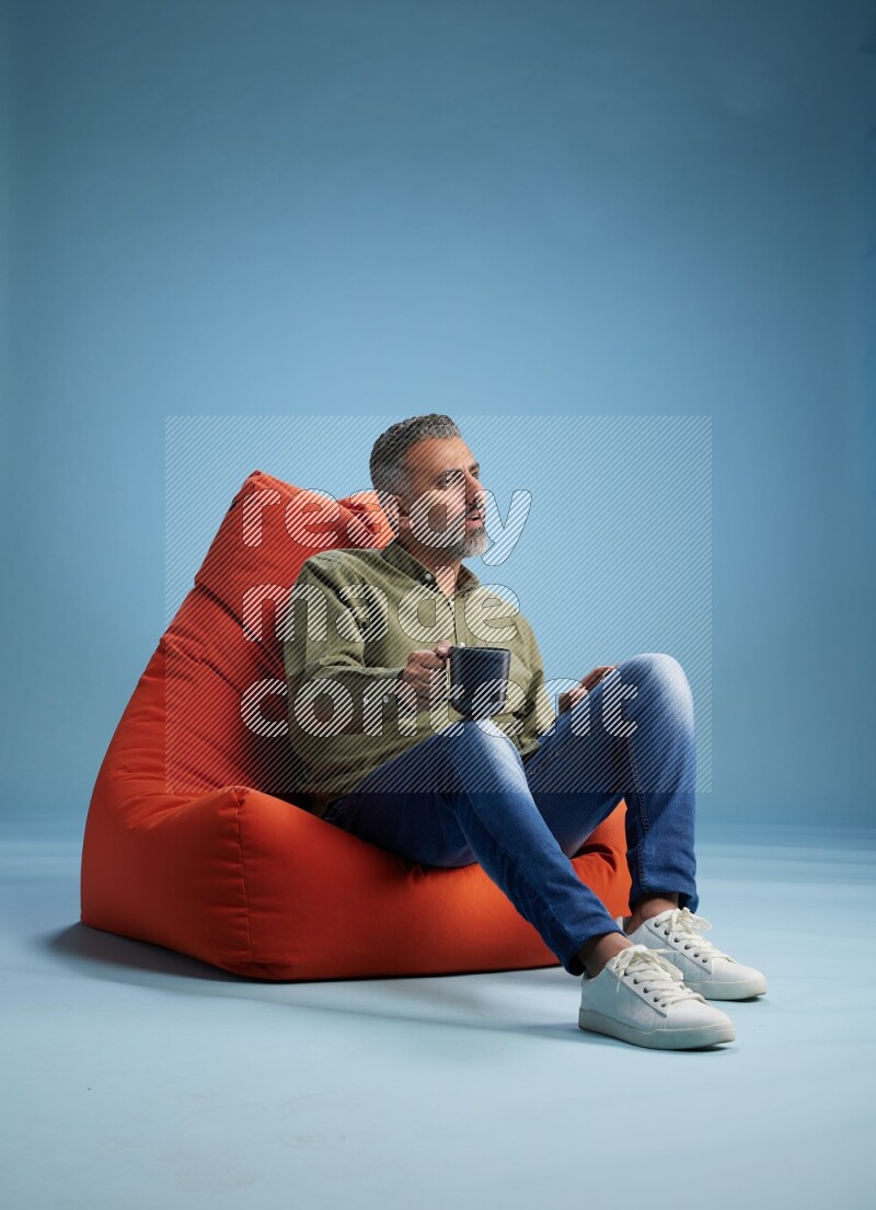 A man sitting on an orange beanbag and drinking coffee