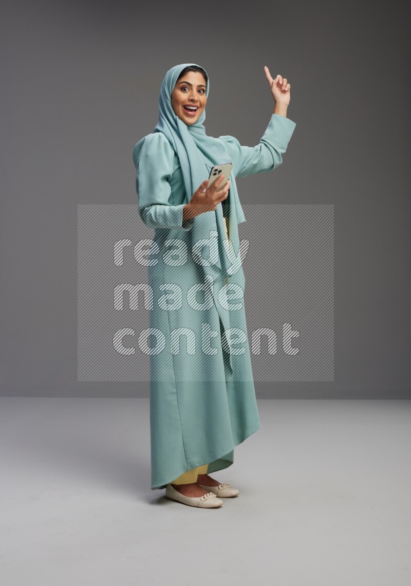 Saudi Woman wearing Abaya standing texting on phone on Gray background