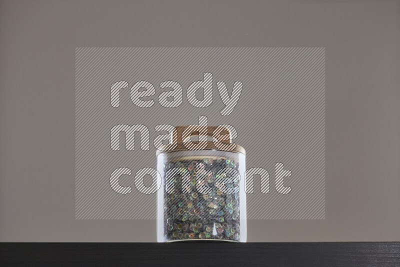 Sequins in a glass jar on black background