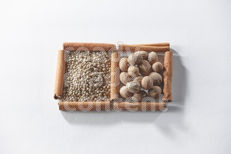 مربعان من أعواد القرفة ممتلئان بحبوب الفلفل الأبيض وجوزة الطيب علي خلفية بيضاء