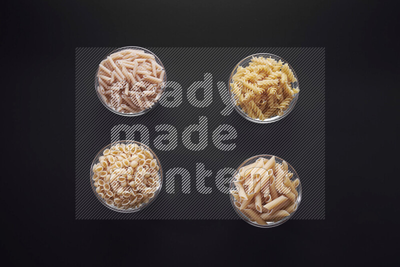 Different pasta types in glass bowls on black background