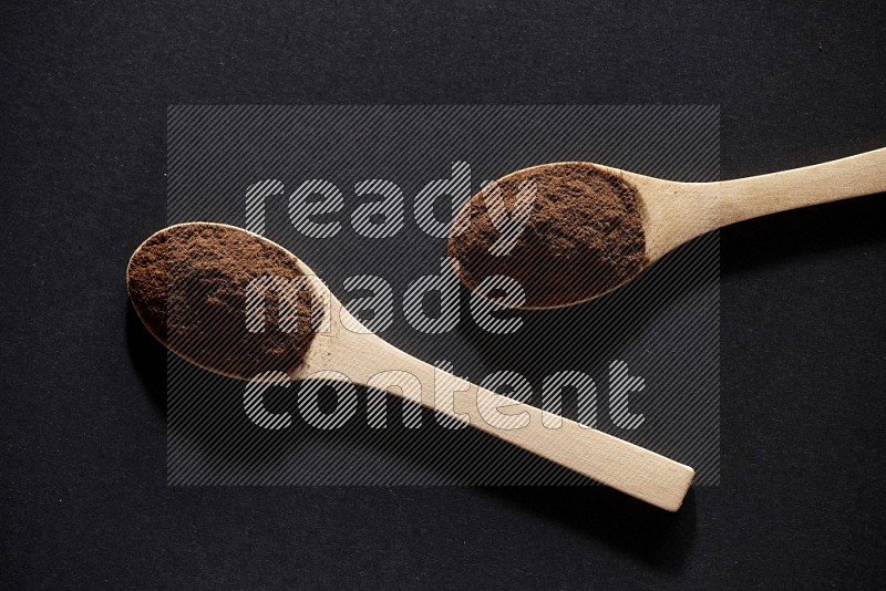 2 wooden spoons full of cloves powder on a black flooring