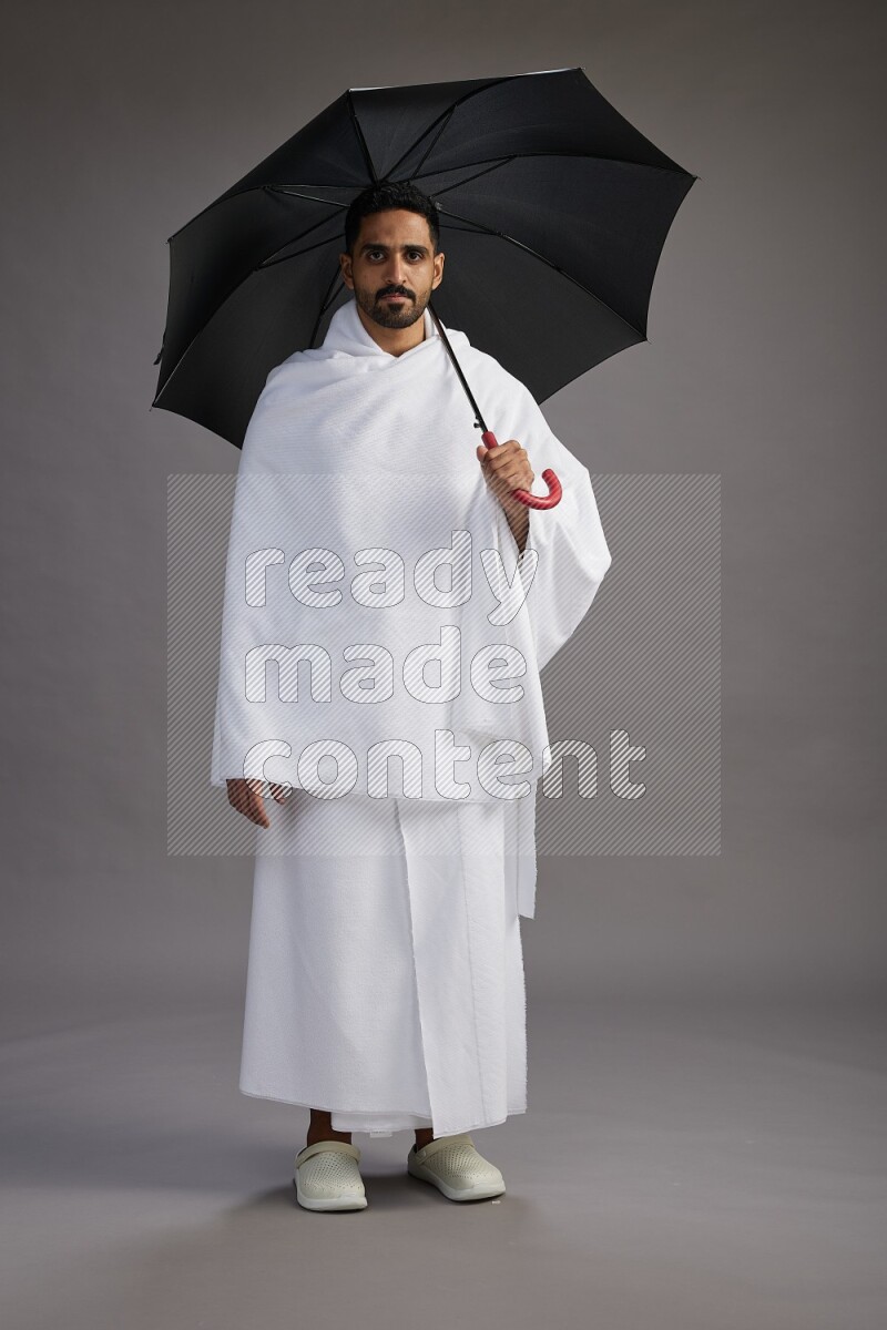A man wearing Ehram Standing holding umbrella on gray background