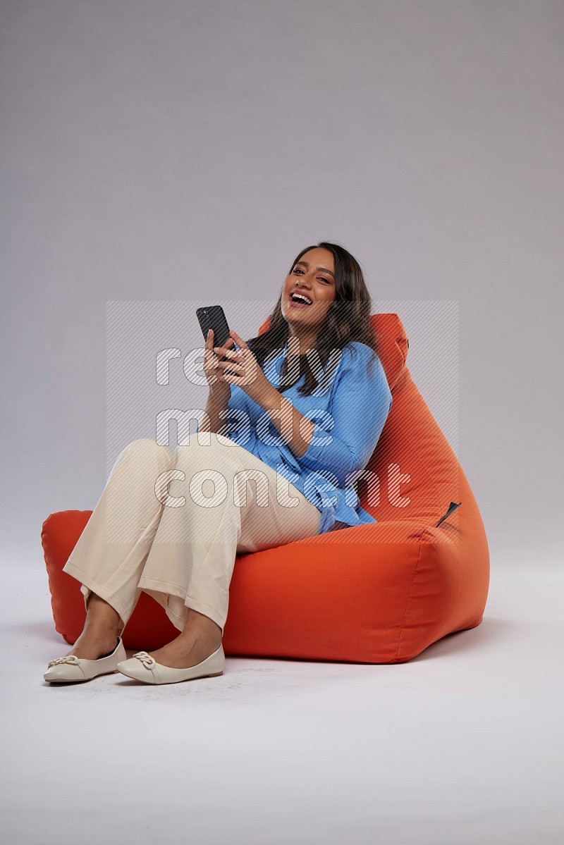 A woman sitting on an orange beanbag and texting on phone