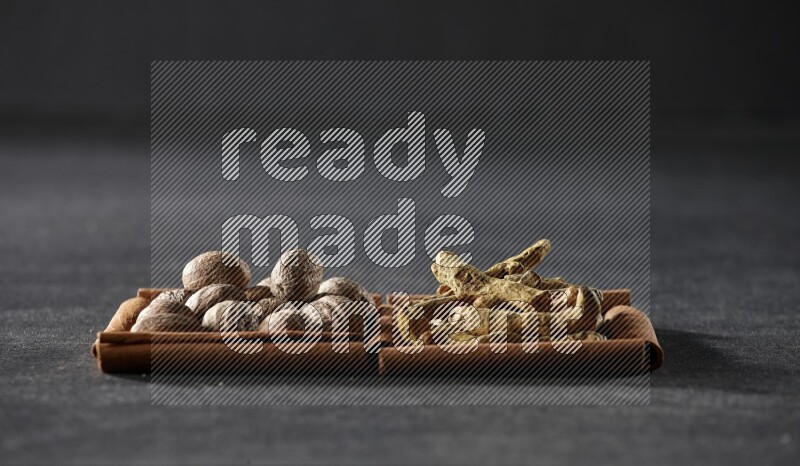 مربعان من أعواد القرفة ممتلئان بجوزة الطيب وأصابع الكركم علي خلفية سوداء