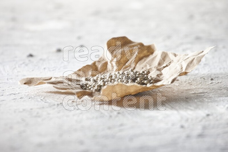 White pepper beads in a crumpled piece of paper on textured white flooring