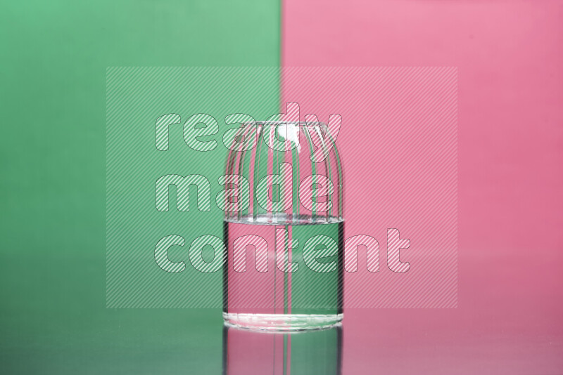 The image features a clear glassware filled with water, set against green and pink background