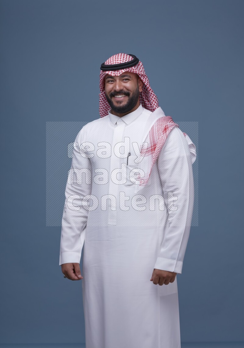 A man pointing on blue background wearing Saudi Thob with Shomag