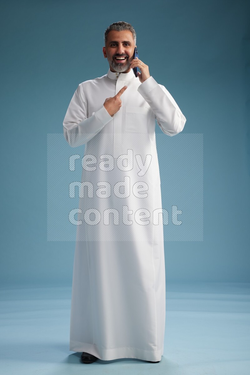 Saudi man wearing thob talking on the phone on blue background