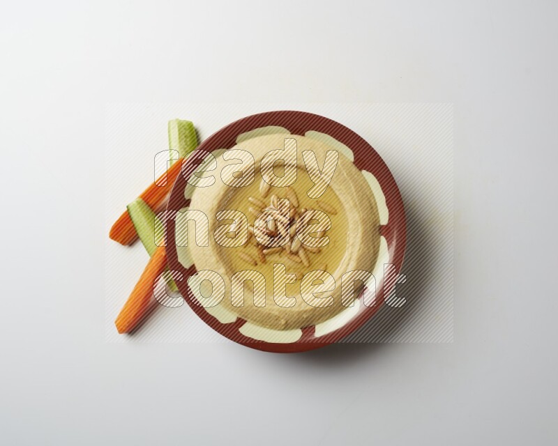 Hummus in a traditional plate garnished with pine nuts on a white background