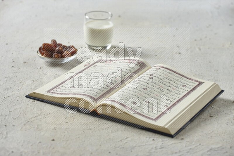 Quran with dates, prayer beads and different drinks all placed on textured white background