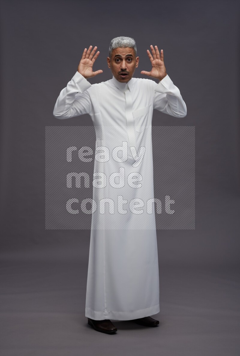 Saudi man wearing thob standing hands behind head on gray background