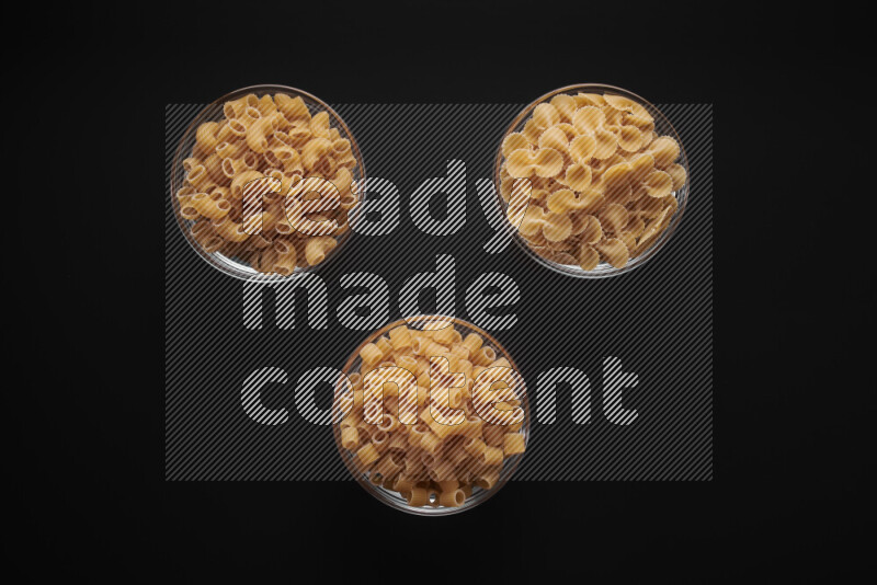 Different pasta types in glass bowls on black background