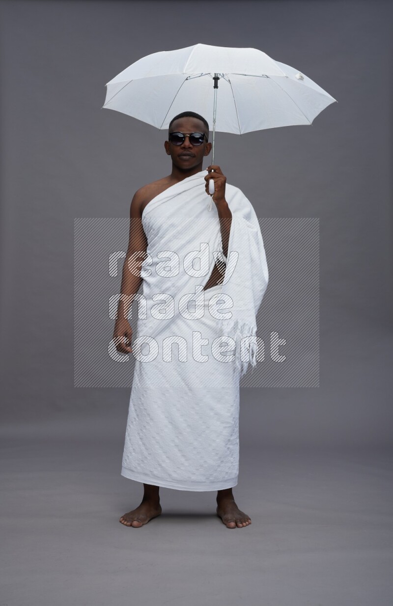 A man wearing Ehram Standing holding umbrella on gray background