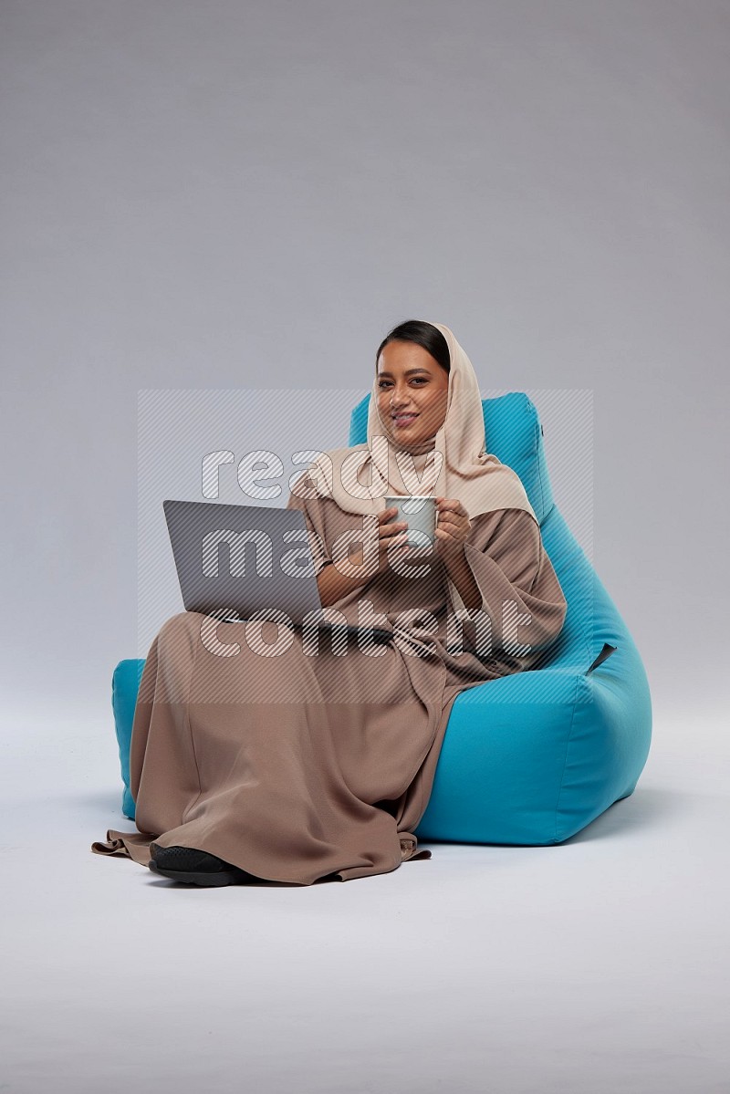 A Saudi woman sitting on a blue beanbag and working on laptop