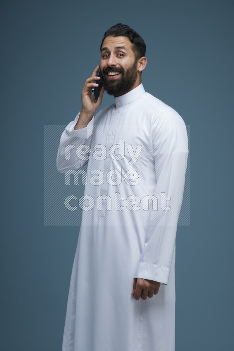 A man having a call on a blue background wearing Saudi Thob