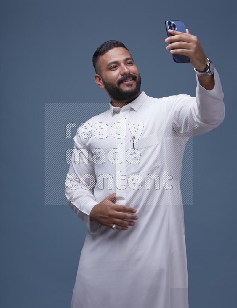 A Saudi man Taking A Selfie on Blue Background wearing Saudi Thob