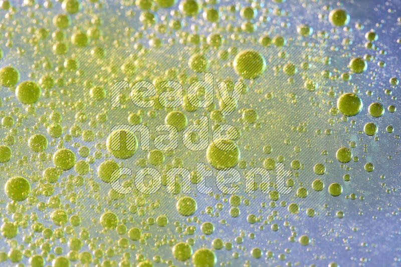 Close-ups of abstract yellow watercolor drops on oil Surface on blue background
