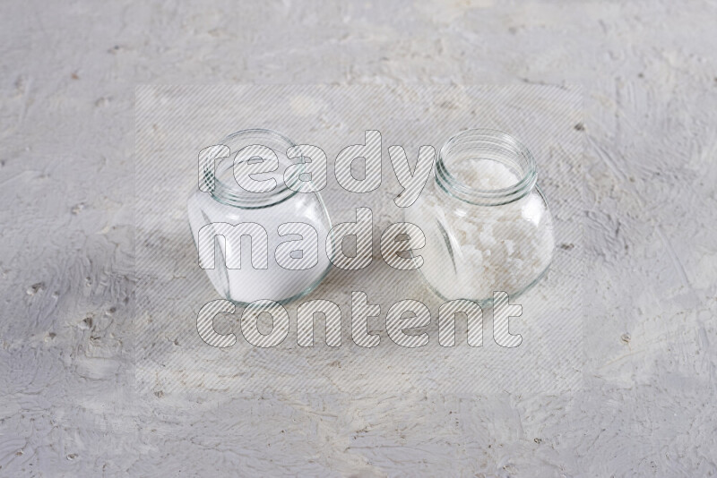 2 glass jars one is filled with table salt and the other with coarse sea salt on white background