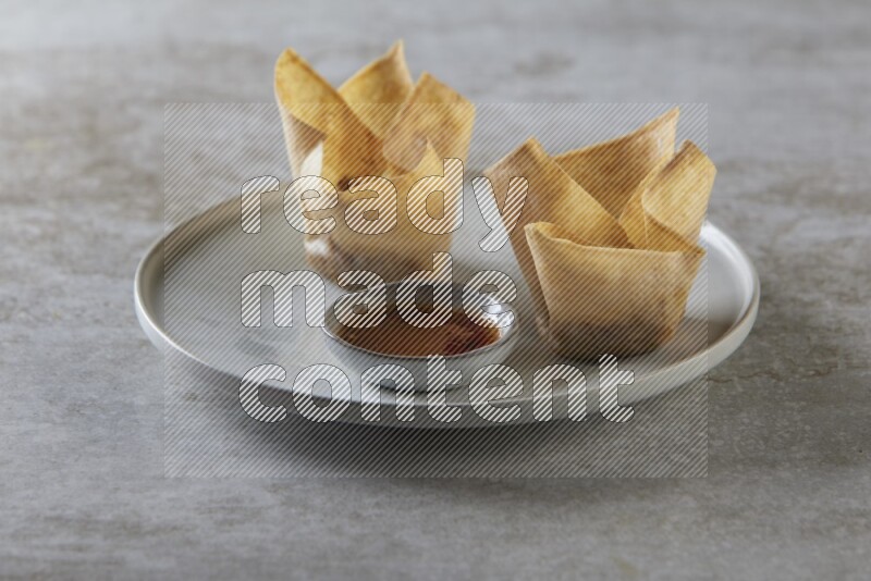wonton cups with soy sauce ramkin on grey ceramic plate on grey textured counter top