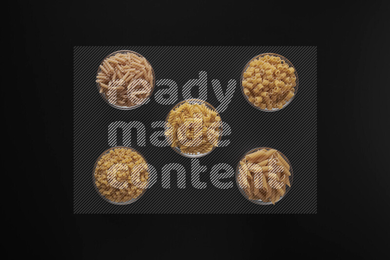 Different pasta types in 5 glass bowls on black background