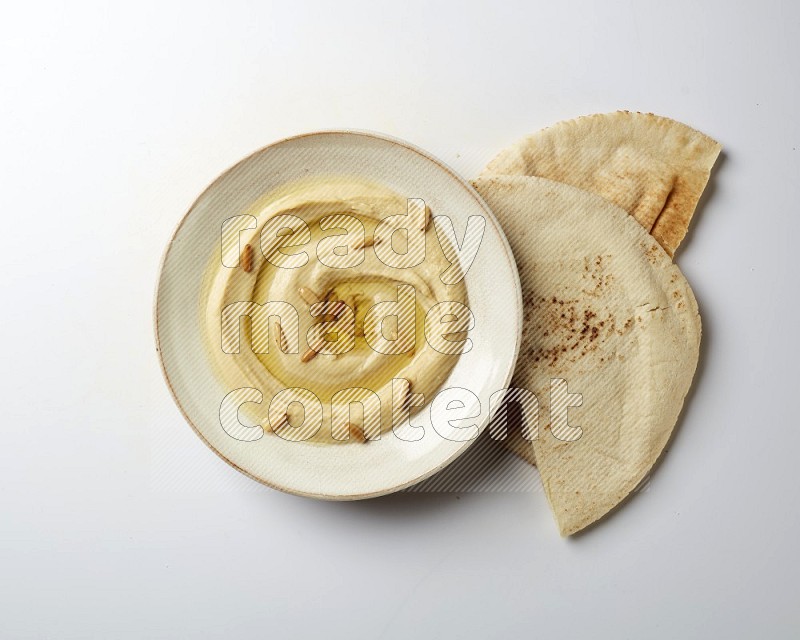 Hummus in a pottry plate garnished with pine nuts on a white background