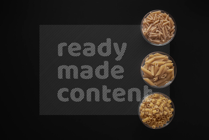 Different pasta types in 3 glass bowls on black background