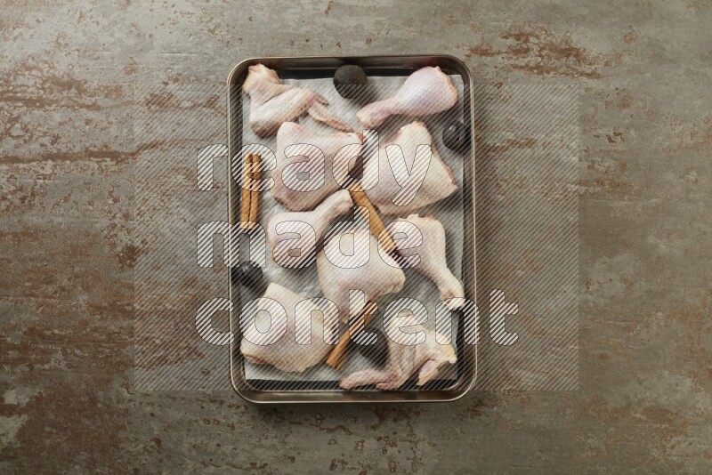 Mixed fresh chicken pieces in an oven tray on a textured rustic background