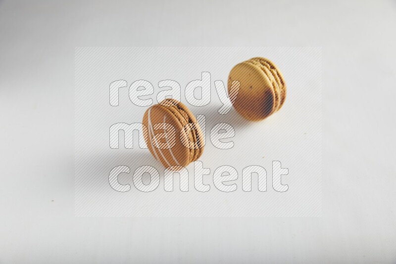 45º Shot of of two assorted Brown Irish Cream, and Yellow Crème Brulée macarons on white background