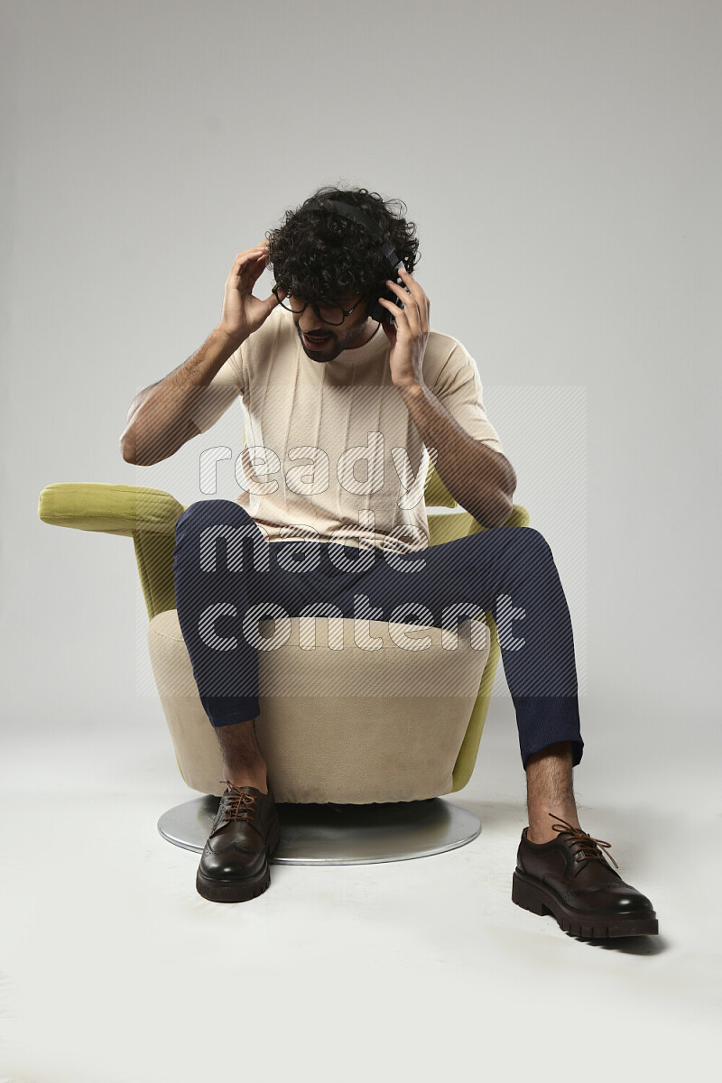 رجل يرتدي ملابس كاجوال يجلس علي كرسي و يضع سماعات رأس علي خلفية بيضاء