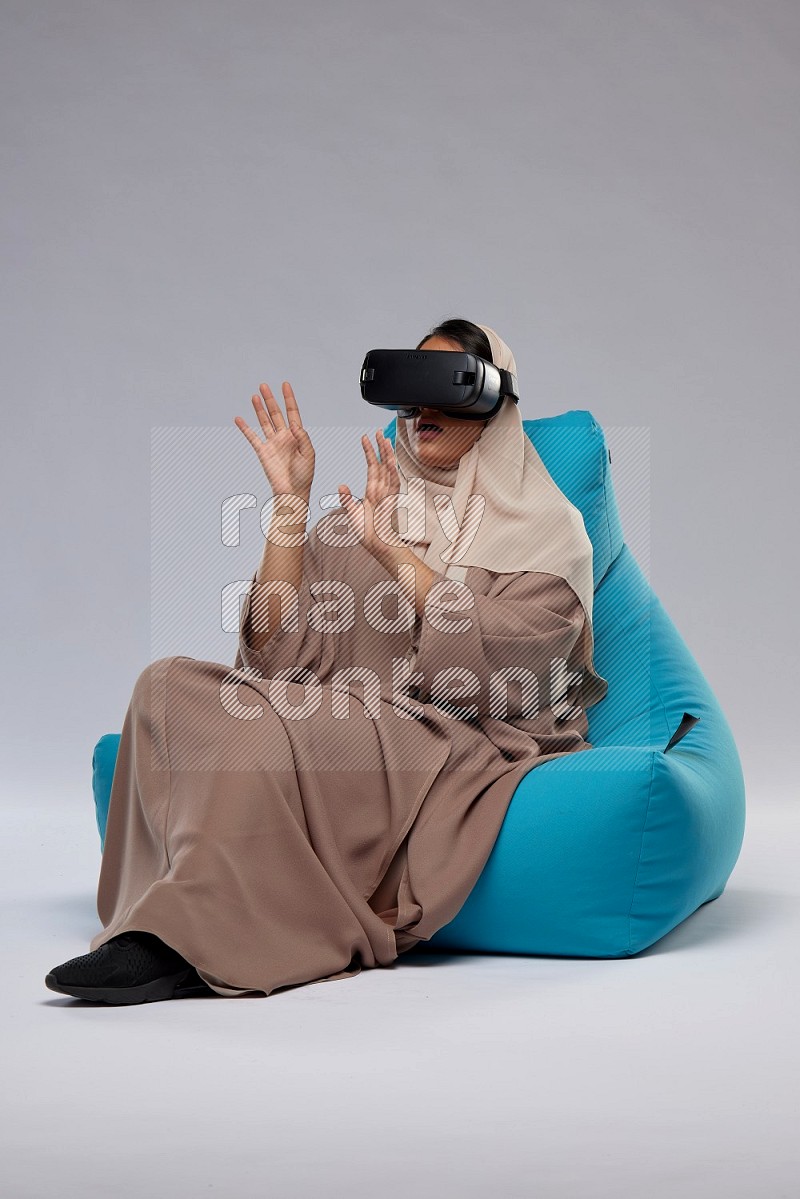 A Saudi woman sitting on a blue beanbag and gaming with VR