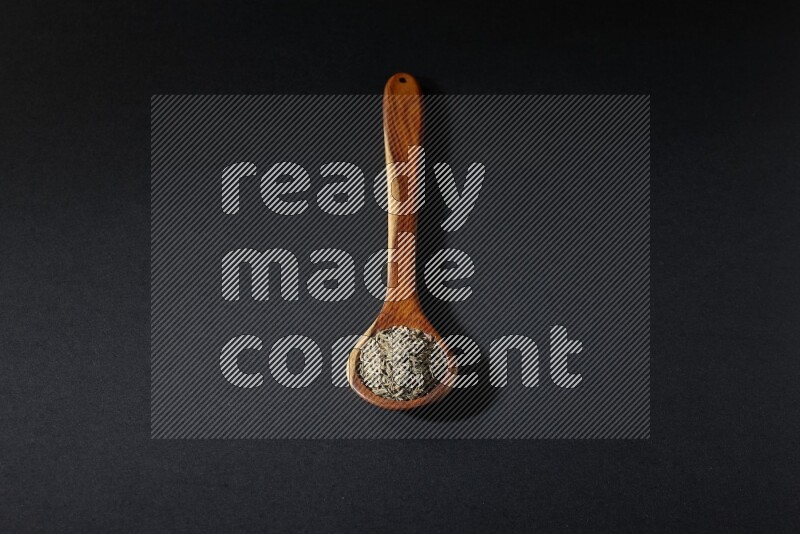 مغرفة خشبية ممتلئة بحبوب الكمون على خلفية سوداء