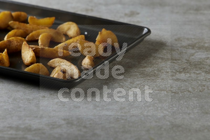 wedges potato in a black stainless steel rectangle tray on grey textured counter top