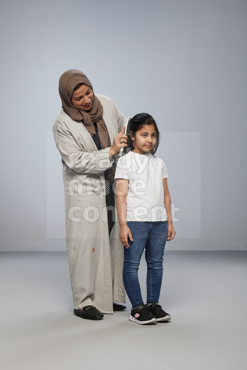 Mom standing styling hair for her daughter on gray background