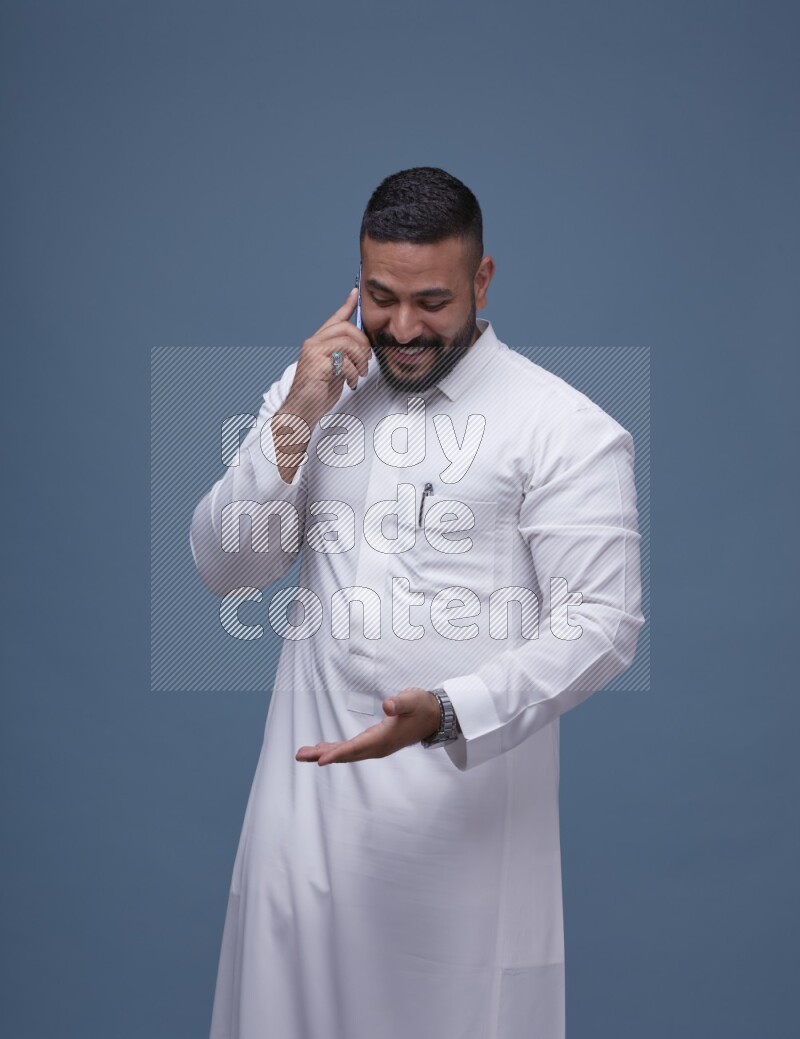 A Saudi man calling on blue background wearing Saudi Thob
