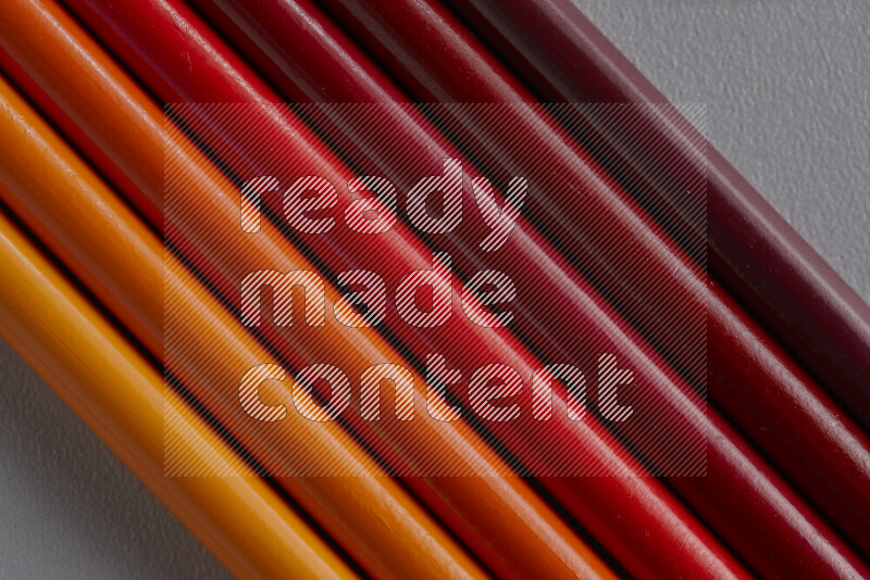 A collection of colored pencils arranged showcasing a gradient of orange and red hues on grey background