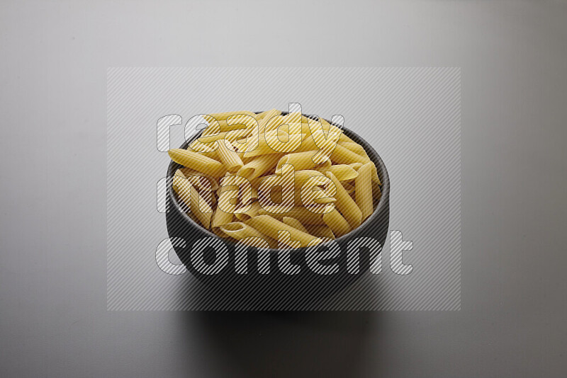Penne pasta in a pottery bowl on grey background