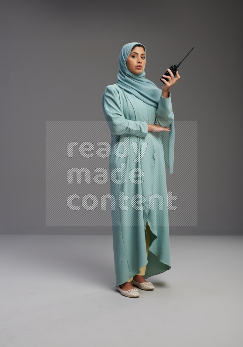 Saudi Woman wearing Abaya standing holding walkie-talkie on Gray background