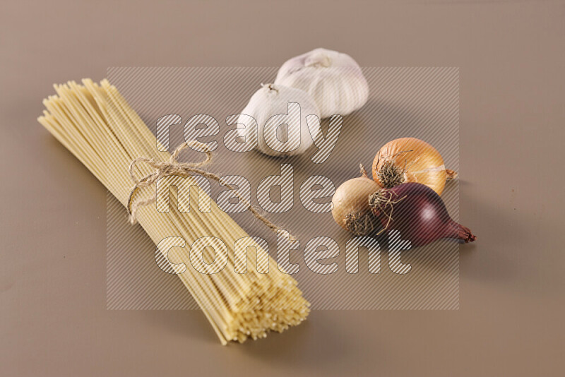 Raw pasta with different ingredients such as cherry tomatoes, garlic, onions, red chilis, black pepper, white pepper, bay laurel leaves, rosemary and cardamom on beige background