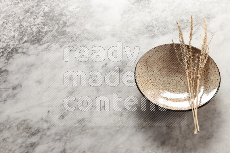 Wheat stalks on multicolored pottery plate on grey marble background